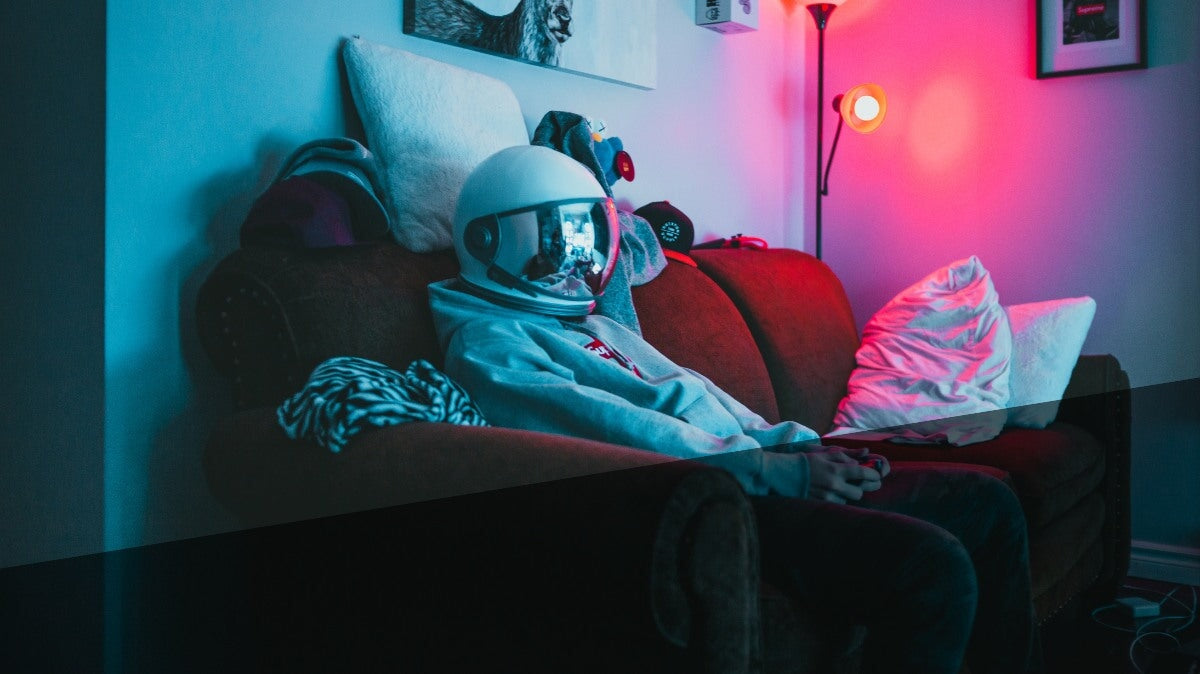 un homme portant un casque spatial assis sur le canapé et jouant à des jeux vidéo